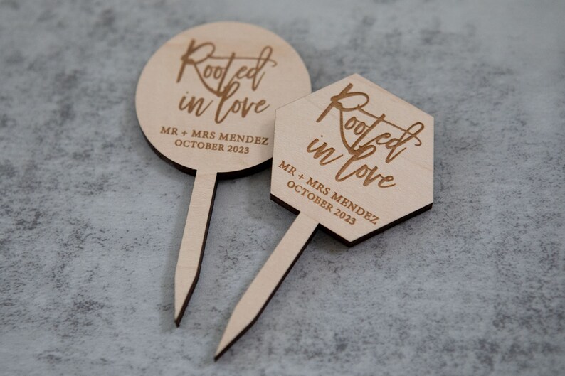 May include: Two wooden cake toppers with the text "Rooted in love" and "MR + MRS MENDEZ OCTOBER 2023".