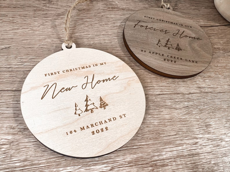 Puede incluir: Dos adornos redondos de madera con un acabado r&uacute;stico. El adorno de la izquierda dice "Primera Navidad en mi nuevo hogar" con una direcci&oacute;n y el a&ntilde;o 2022. El adorno de la derecha dice "Primera Navidad en nuestro hogar para siempre" con una direcci&oacute;n y el a&ntilde;o 2022.