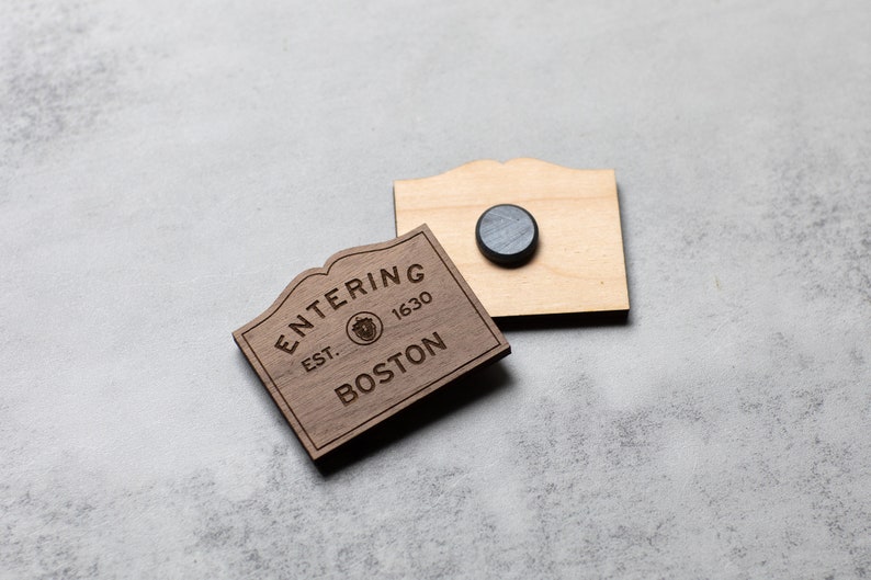 May include: Wooden sign with the text "Entering Est. 1630 Boston" with a small graphic of a tree. The sign is attached to a wooden backing with a magnet.