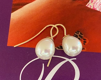May include: A pair of gold-colored drop earrings featuring large, pearlescent white teardrop-shaped pearls. The earrings have a simple, elegant design with a hook closure. The background is a mix of orange, red, and purple.