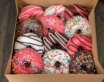May include: A box filled with a variety of donuts. The donuts are topped with chocolate, sprinkles, and pink frosting.