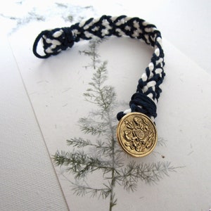 Braid and Button Cuff of Navy and White Silk Cords with a Brass Button Closure with a Coat of Arms Motif