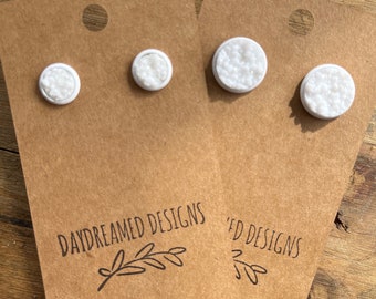 May include: Two pairs of white stud earrings with a textured, crystalline surface, each mounted on a brown cardboard display card labeled with the text DAYDREAMED DESIGNS and a small leaf illustration at the bottom of the card.