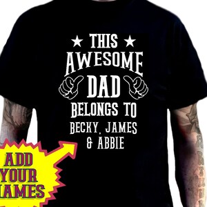 May include: Black t-shirt with the text "THIS AWESOME DAD BELONGS TO BECKY, JAMES & ABBIE" in white. The design includes thumbs up and star graphics. Additional shirt colours are shown in the image.