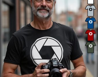 Może przedstawiać: Mężczyzna w czarnej koszulce z białym wzorem przysłony, trzymający czarny aparat fotograficzny. Obraz pokazuje również ten sam wzór na białych, szarych, niebieskich, czerwonych i zielonych koszulkach. Mężczyzna jest na zewnątrz.