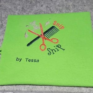 May include: Green t-shirt with an embroidered design of scissors and a comb with the text "snip snip snip" and "by Tessa".