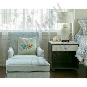 May include: A light blue chaise lounge with a decorative pillow featuring embroidered flip-flops in blue, green, and orange. A white lamp sits on a nightstand next to a bed with a patterned comforter. The room has sheer curtains.