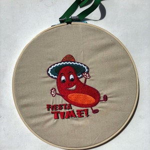 May include: Embroidered hoop art featuring a red chili pepper wearing a sombrero and the text "Fiesta Time!"