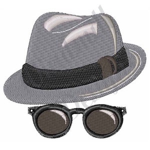 Op de afbeelding: Een grijze fedora-hoed met een zwarte band en een bruine gesp. De hoed is naar de zijkant gekanteld. Onder de hoed bevindt zich een paar zwarte ronde zonnebrillen met donkere glazen.