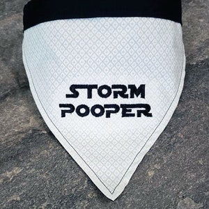 May include: White dog bandana with black trim and the text "STORM POOPER" embroidered in black.