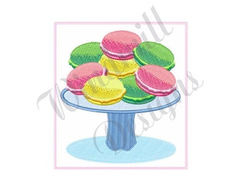 May include: A blue pedestal cake stand with a white base and a blue pedestal. The stand is filled with colorful macarons in shades of pink, green, and yellow.