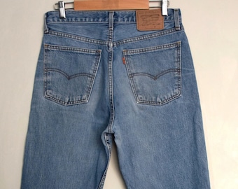 May include: A pair of blue denim jeans with a brown leather patch on the back pocket. The patch has the text "Levi's" and "Original  Fit" on it.