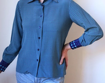May include: A blue and black patterned long-sleeved shirt with a collared neckline and button closure. The shirt has blue and white polka dot cuffs.