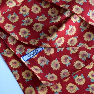 May include: Red fabric with a repeating pattern of yellow sunflowers. The fabric has a white label with the word "Codello" printed in black.