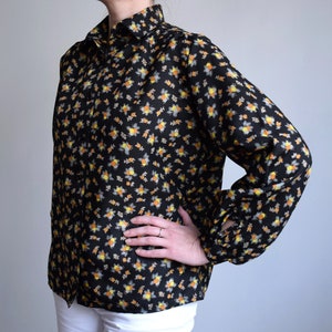 Puede incluir: Una blusa negra de manga larga con estampado floral en tonos amarillos y naranjas.
