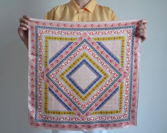 May include: A pink silk scarf with a geometric pattern in shades of red, yellow, blue, and black. The pattern features a central diamond shape surrounded by multiple borders.