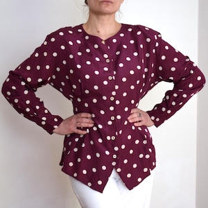 May include: A long-sleeved button-up blouse with a burgundy background and white polka dots. The blouse has a fitted waist and a slightly flared hem.