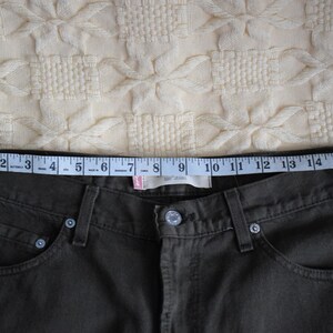 May include: A pair of dark green jeans with a measuring tape across the waistband. The tape reads 17 inches.