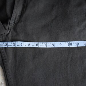 May include: A dark green pair of pants with a measuring tape across the bottom. The tape reads 1 to 14 inches.