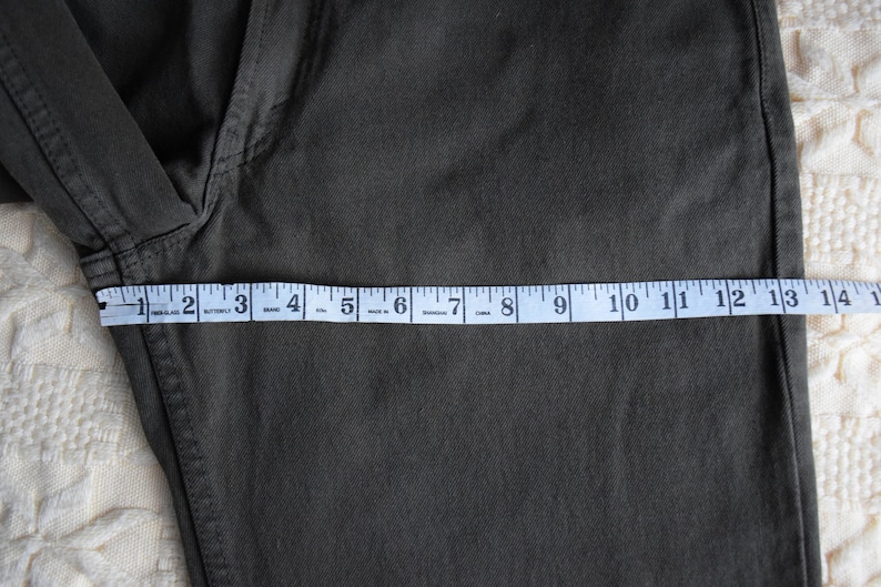May include: A dark green pair of pants with a measuring tape across the bottom. The tape reads 1 to 14 inches.