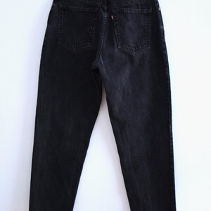 Peut inclure: Un jean en denim noir, suspendu &agrave; un cintre en bois. Le jean a deux poches arri&egrave;re et une &eacute;tiquette rouge et blanche. Le denim semble l&eacute;g&egrave;rement d&eacute;lav&eacute;.