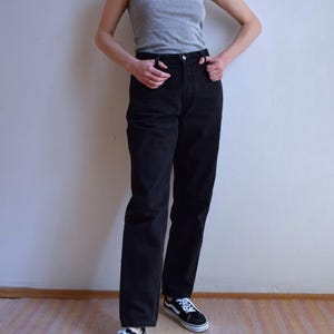 Peut inclure: Une personne porte un d&eacute;bardeur gris, un jean noir et des baskets noires et blanches. La tenue est simple et d&eacute;contract&eacute;e, adapt&eacute;e au quotidien. Les baskets ont des lacets blancs et une bande blanche.