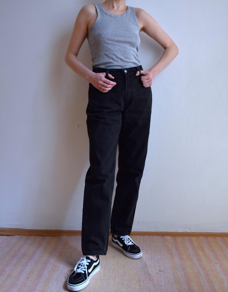 Peut inclure: Une personne porte un d&eacute;bardeur gris, un jean noir et des baskets noires et blanches. La tenue est simple et d&eacute;contract&eacute;e, adapt&eacute;e au quotidien. Les baskets ont des lacets blancs et une bande blanche.