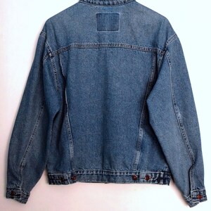Puede incluir: Una chaqueta vaquera azul con cierre de botones y dos bolsillos en la parte delantera. La chaqueta tiene un estilo cl&aacute;sico y est&aacute; hecha de un material duradero.