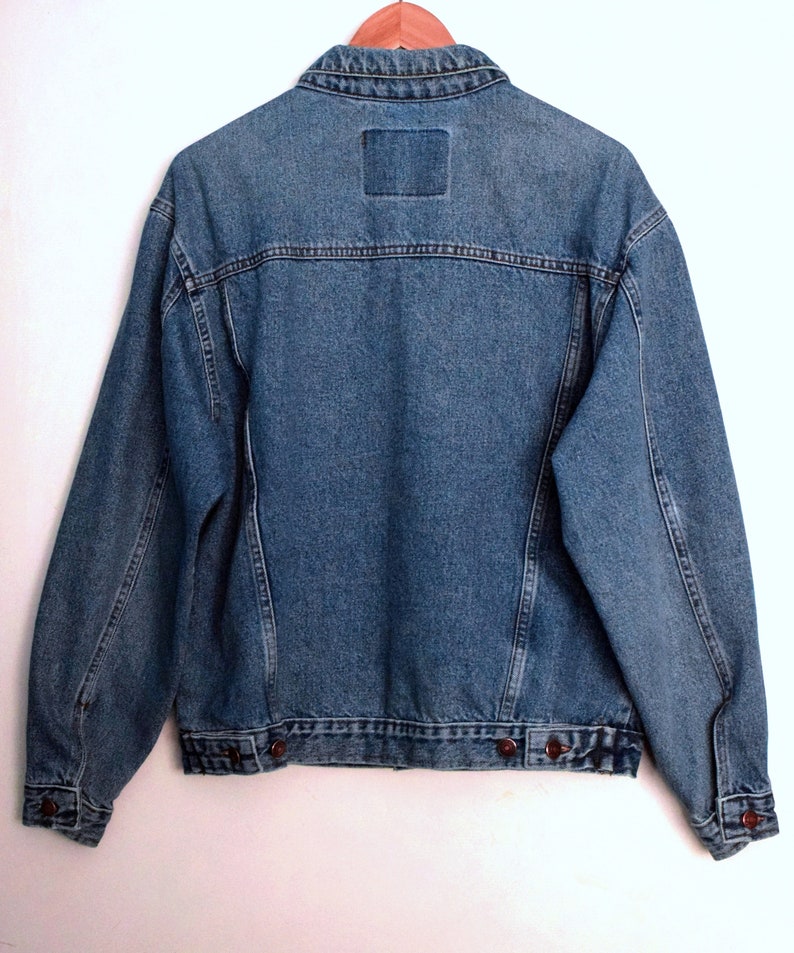 Puede incluir: Una chaqueta vaquera azul con cierre de botones y dos bolsillos en la parte delantera. La chaqueta tiene un estilo cl&aacute;sico y est&aacute; hecha de un material duradero.