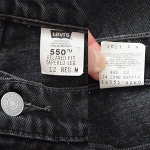 Peut inclure: Gros plan sur un jean noir Levi's 550 Relaxed Fit Tapered Leg. Le jean a une fermeture &agrave; bouton et une &eacute;tiquette blanche avec le logo Levi's et des informations de taille. L'&eacute;tiquette indique la taille "12 REG. M".