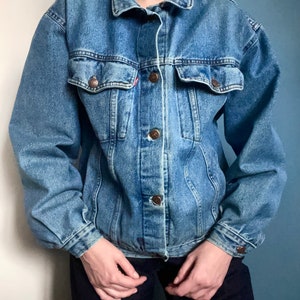Puede incluir: Una chaqueta vaquera azul cl&aacute;sica con cierre de botones y dos bolsillos con solapa. La chaqueta tiene un corte holgado y est&aacute; hecha de una tela vaquera suave y c&oacute;moda.