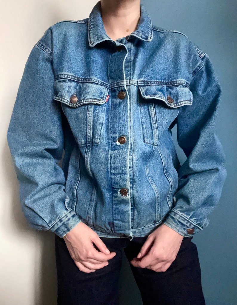 Puede incluir: Una chaqueta vaquera azul cl&aacute;sica con cierre de botones y dos bolsillos con solapa. La chaqueta tiene un corte holgado y est&aacute; hecha de una tela vaquera suave y c&oacute;moda.