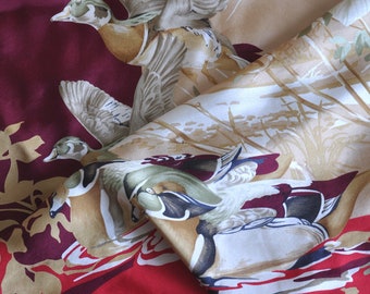 May include: A red, brown, and beige fabric with a repeating pattern of flying ducks. The ducks are depicted in a realistic style with detailed feathers and beaks.
