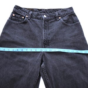 Peut inclure: Gros plan sur un jean en denim noir avec un ruban &agrave; mesurer bleu sur la taille. Le jean a une conception classique &agrave; cinq poches et une fermeture &agrave; bouton et &agrave; glissi&egrave;re. La taille mesure environ 61 cm.