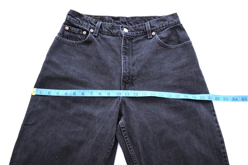 Peut inclure: Gros plan sur un jean en denim noir avec un ruban &agrave; mesurer bleu sur la taille. Le jean a une conception classique &agrave; cinq poches et une fermeture &agrave; bouton et &agrave; glissi&egrave;re. La taille mesure environ 61 cm.
