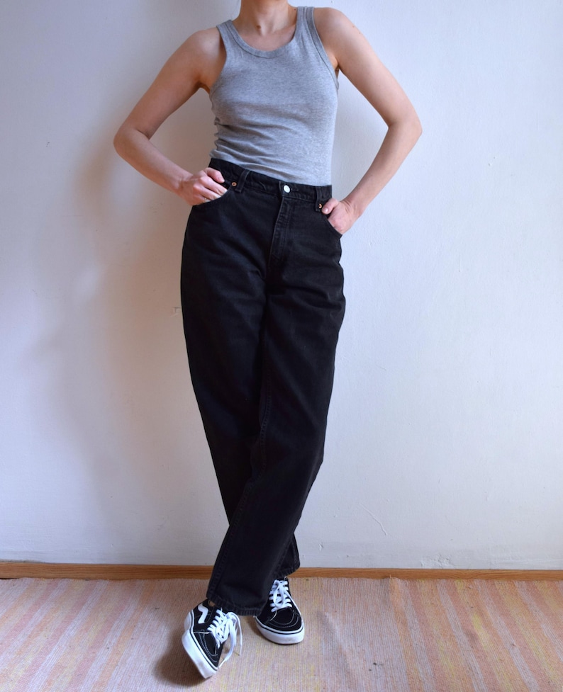 Peut inclure: Une personne porte un d&eacute;bardeur gris, un jean noir et des baskets noires et blanches. Le jean est taille haute et les baskets ont des lacets blancs. La personne se tient debout, les bras le long du corps.