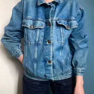 Puede incluir: Una chaqueta vaquera azul cl&aacute;sica con cierre de botones y dos bolsillos de solapa. La chaqueta tiene un aspecto desgastado y est&aacute; hecha de una tela suave y c&oacute;moda.