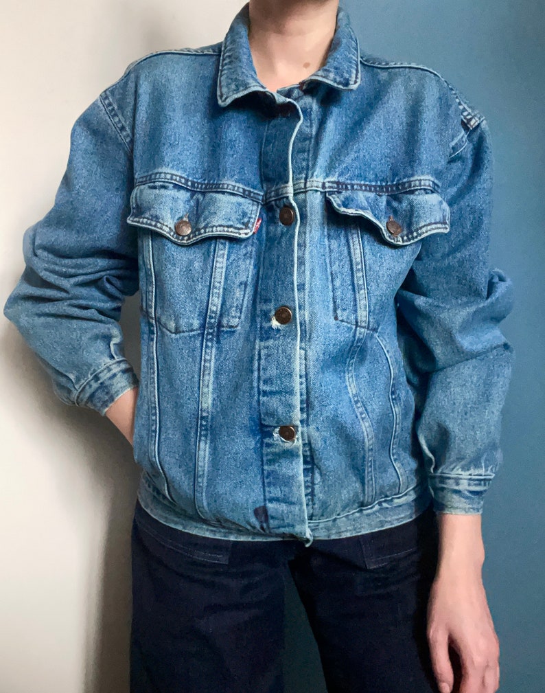 Puede incluir: Una chaqueta vaquera azul cl&aacute;sica con cierre de botones y dos bolsillos de solapa. La chaqueta tiene un aspecto desgastado y est&aacute; hecha de una tela suave y c&oacute;moda.
