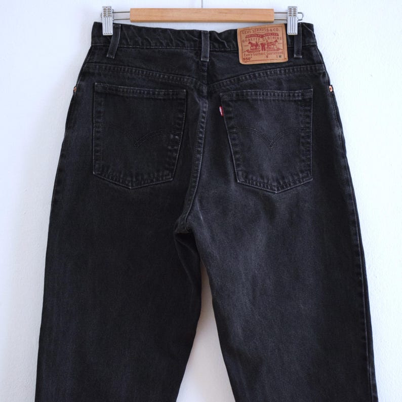 Peut inclure: Jean noir en denim avec une conception classique &agrave; cinq poches. Le jean pr&eacute;sente une &eacute;tiquette rouge Levi's sur la poche arri&egrave;re et est suspendu &agrave; un cintre en bois. Le jean est d&eacute;lav&eacute; fonc&eacute; et semble vintage.