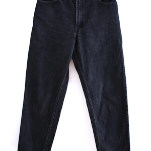 Peut inclure: Jean en denim noir avec une conception classique &agrave; cinq poches. Le jean est suspendu &agrave; un cintre en bois sur fond blanc. Fermeture boutonn&eacute;e, passants de ceinture et rivets en cuivre. Aspect l&eacute;g&egrave;rement d&eacute;lav&eacute;.