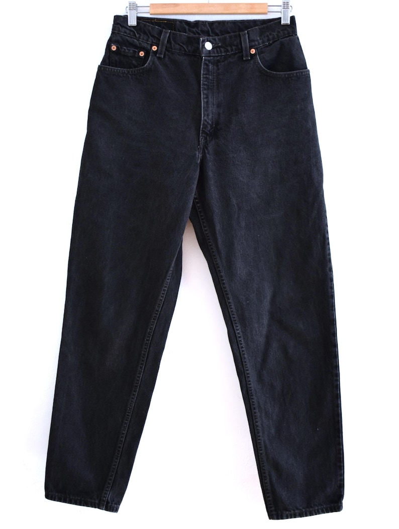 Peut inclure: Jean en denim noir avec une conception classique &agrave; cinq poches. Le jean est suspendu &agrave; un cintre en bois sur fond blanc. Fermeture boutonn&eacute;e, passants de ceinture et rivets en cuivre. Aspect l&eacute;g&egrave;rement d&eacute;lav&eacute;.