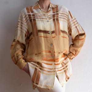 May include: A cream, tan, and brown patterned button-down shirt. The long-sleeved shirt features a collared neckline and is buttoned. The shirt is made of a lightweight material and has a relaxed fit, suitable for various occasions.