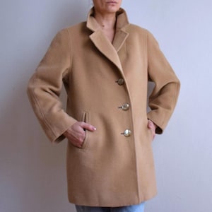 May include: A tan wool coat with a classic design. The coat features a notched collar, three gold-coloured buttons, and two front pockets. The coat is knee-length and has long sleeves.
