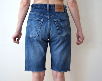 May include: A pair of blue denim shorts with a frayed hem. The shorts have a classic five-pocket design and a brown leather patch on the back.
