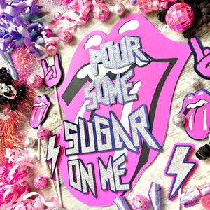 May include: Pink and black party decorations with a large pink tongue cutout with the text "Pour Some Sugar On Me".