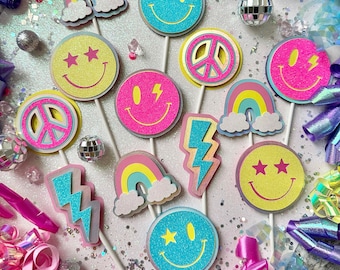 May include: Assortment of colorful party decorations with a 70s theme. The decorations include peace signs, smiley faces, rainbows, lightning bolts, and stars. The decorations are made of glitter paper and have a holographic finish.