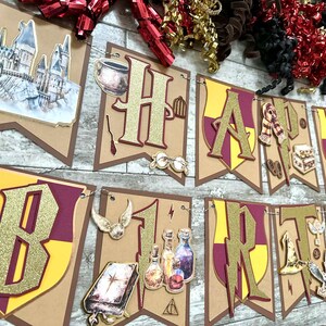 May include: A 'Happy Birthday' banner with gold glitter lettering on brown pennants. Each pennant features a burgundy and yellow shield design. The banner is decorated with themed images, including a castle, glasses, and a scarf.