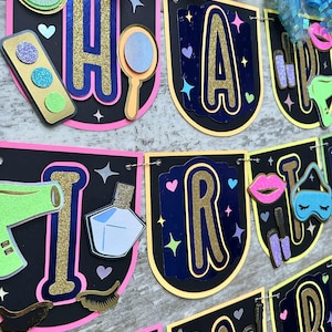 May include: A decorative banner spelling "HAPPY BIRTHDAY" with beauty-themed embellishments. The letters are gold with a navy blue background, outlined in yellow and pink. The decorations include a mirror, lipstick, and eye shadow.