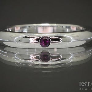 May include: A polished silver ring with a single, oval-shaped, deep purple gemstone set in the center. The ring's surface reflects the surrounding environment, creating a mirrored effect. The ring is a piece of jewelry.