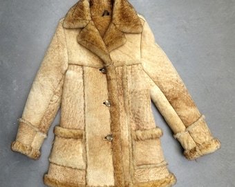May include: A vintage beige shearling coat with a notched collar, button closure, and two front pockets. The coat features a patchwork design with brown trim and cuffs. A warm winter coat.